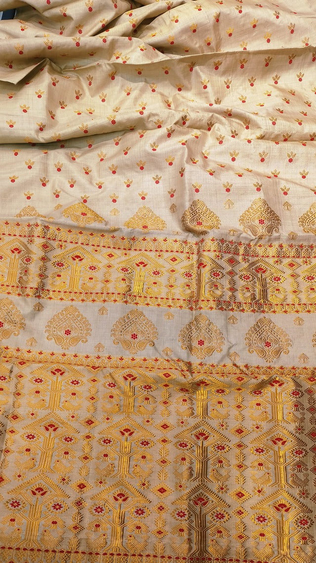 Front view of Assam handloom Muga silk saree with a cream-beige ground, gold-toned motifs and red floral accents.