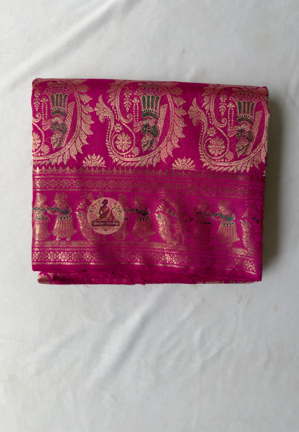Close-up of pallu of pink Swarnachari pure silk saree showing golden zari mythology and Bishnupur temple art compositions luminous and celebratory against festive pink silk ground