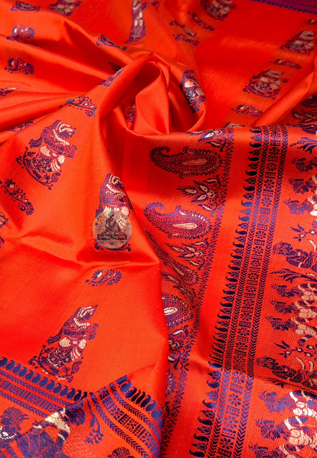 Full saree view of orange Baluchari silk saree with patterned body, contrasting borders and decorative pallu