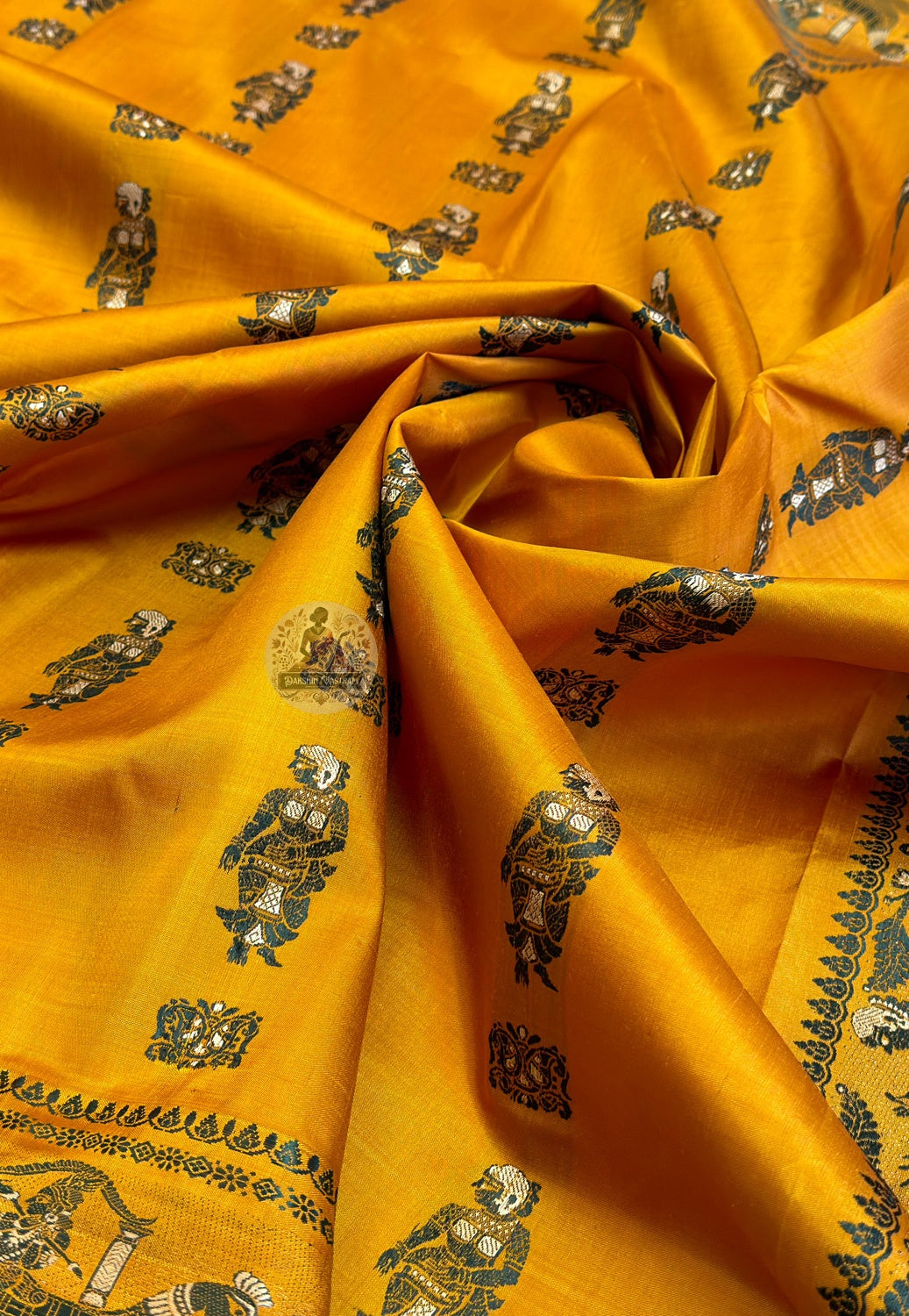 Macro detail of mustard Baluchari silk fabric showing hand-woven figurative butidar motifs of royal figures and the lustrous texture of pure silk