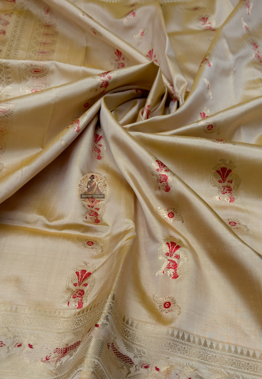 Close up of beige gold Swarnachari silk saree pallu with red figures beneath arch-shaped frames
